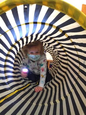 Child holding flashlight with mask bravely goes through a cloth, black and white striped tunnel 